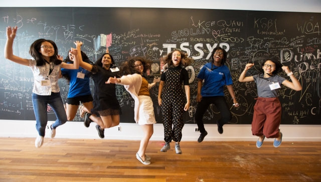 ISSYP class of 2019 jumping in front of a blackboard covered in doodles