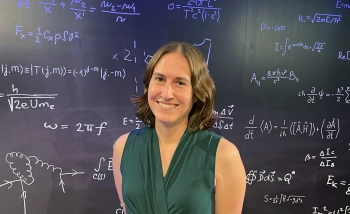 Woman wearing a green shirt standing in front of a blackboard of equations