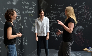 Three women surrounded by chalkboards with equations